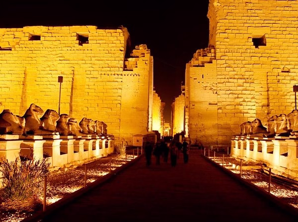 Towering ancient stone columns in the Great Hypostyle Hall at Karnak Temple, Luxor, featuring detailed colorful hieroglyphs and carvings of Egyptian deities under a clear blue sky.