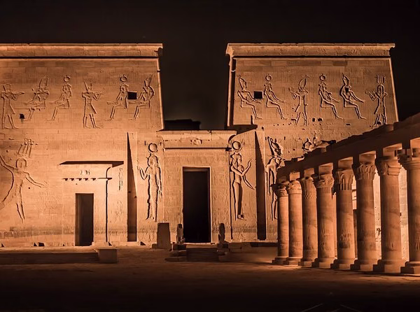 The grand facade of Philae Temple illuminated at night, featuring ancient reliefs and columns for Egypt travel.