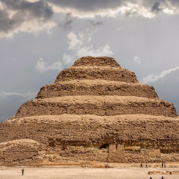The ancient Step Pyramid of Djoser at Saqqara under a cloudy sky, a historic landmark for travelers in Egypt.
