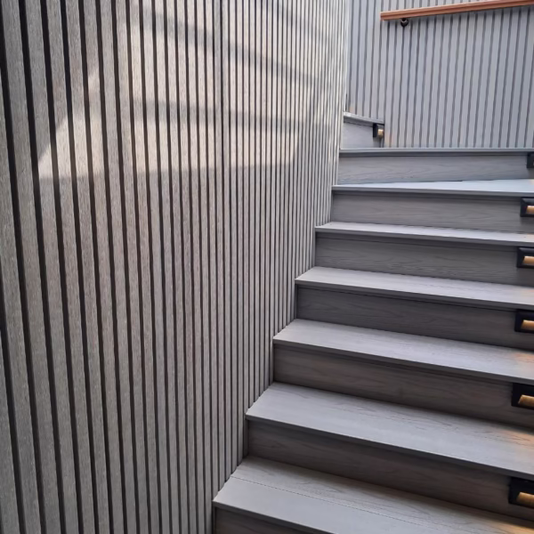 A modern outdoor staircase on a luxury cruise ship featuring grey wood-textured steps, vertical slat wall paneling, and integrated LED step lighting for safety and ambiance.