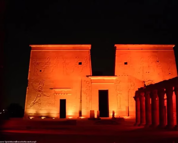 Philae Temple's First Pylon bathed in vibrant red light at night, a dramatic ancient Egyptian travel destination.