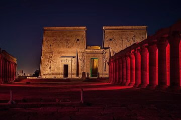 The Temple of Philae in Aswan glowing with red and gold lights at night, a dramatic scene for Egypt travel.