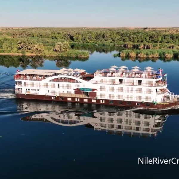 Luxury Nile cruise ship sailing on calm water with desert and palm tree reflections for an Egypt river travel tour.