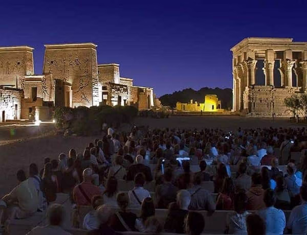 Crowd of tourists watching an illuminated night show at the Philae Temple, a top experience for travel in Egypt.